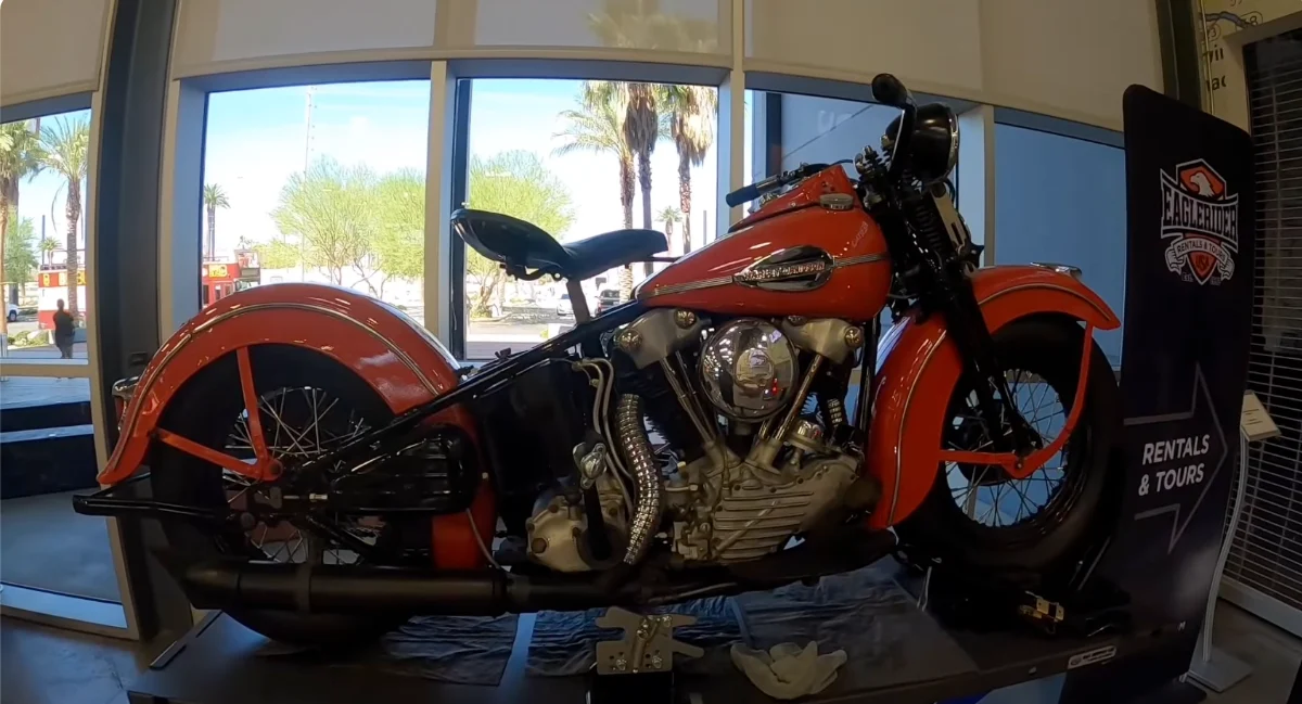 A vintage orange and black Harley-Davidson motorcycle from the 1940s era displayed on a platform in Las Vegas